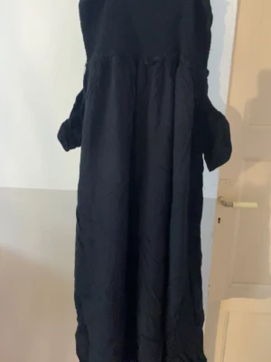 Svart långklänning från Ellos - Säljer en svart långklänning från Ellos med vida ärmar och lös passform. Klänningen har en enkel design och är tillverkad i ett mjukt tyg som faller snyggt. Perfekt för dig som gillar en stilren och bekväm look.