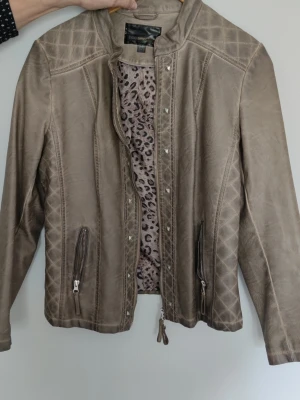 Beige skinnjacka  - Beige skinnjacka med quiltade detaljer på axlar och rygg. Jackan har dragkedja fram och ett leopardmönstrat innerfoder. Rak passform och ståkrage.
