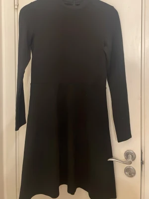 Svart långärmad klänning - En stilren svart klänning med lång ärm och rund hals. Klänningen har en enkel, rak passform och slutar strax ovanför knäna. Perfekt för dig som gillar minimalistisk stil och vill ha något klassiskt i garderoben.
