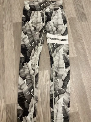 Svarta och vita leggings med bladmotiv - Snygga leggings med svartvitt bladmönster och hög midja. Tight passform och stretchigt material som sitter skönt. Perfekta för dig som gillar att sticka ut med coola prints.