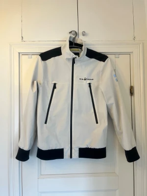 Sail Racing-jacka M - Vit jacka med svarta detaljer från Sail Racing. Finns såklart tecken på användning men allt är helt och jacken ger ett väldigt bra intryck. Storlek M.