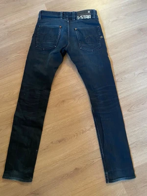 Mörkblå jeans från G-Star - Snygga mörkblå jeans från G-Star med klassiska fem fickor och kontrastsömmar. Jeansen har en smal passform och G-Star-logga på linningen bak. Tillverkade i denim.
