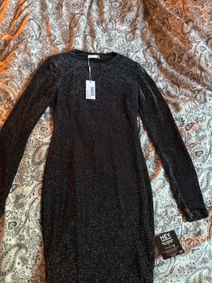 Svart glittrig klänning NLY Trend - Snygg svart glittrig klänning från NLY Trend i figurnära modell. Klänningen har långa ärmar och rund halsringning. Perfekt för dig som vill sticka ut med lite extra glitter. Materialet känns mjukt och stretchigt. Aldrig använd o alla prislappar o lappar kvar!!