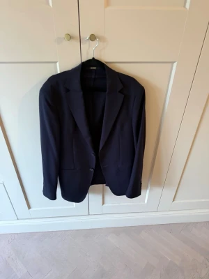Mörkblå ullkavaj Massimo Dutti - Stilren mörkblå kavaj från Massimo Dutti i 100% ull. Klassisk modell med två knappar framtill, fickor och snygg passform. Perfekt för dig som vill ha en tidlös och dressad look. Italienskt tyg och diskreta detaljer.