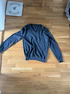 Mörkgrå V-ringad tröja Ben Sherman - Mörkgrå V-ringad tröja från Ben Sherman. Tröjan har långa ärmar, ribbade muddar och är tillverkad i ett mjukt, tunt material som passar perfekt till lager på lager. Klassisk och stilren design som funkar till det mesta.