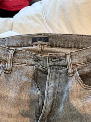 Grå jeans från Polo Ralph Lauren - Snygga grå jeans från Polo Ralph Lauren med klassisk femficksmodell och svart läderpatch bak i midjan. Jeansen har raka ben och är tillverkade i slitstark denim. Perfekta för en avslappnad och trendig look. Storlek:30/32