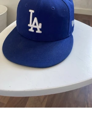 Blå LA Dodgers keps från New Era - Snygg blå keps från New Era med LA Dodgers-logga broderad i vitt framtill. Klassisk modell med rak skärm och ventilationshål. Kepsen har även New Era-loggan broderad på sidan. Perfekt för dig som gillar sportig streetstyle.