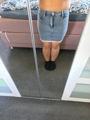 Blå jeanskjol med rå kant - Säljer en blå jeanskjol i klassisk modell med rå, fransig kant nertill. Kjolen har fem fickor, bälteshällor och stängs med knapp och dragkedja framtill. Perfekt till sommaren och enkel att matcha med olika toppar. Den är omsydd först var det ett par jeans 