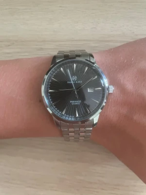 Pablo Raez silverfärgad klocka - Stilren klocka från Pablo Raez med silverfärgad länkarmband i metall och svart urtavla. Klockan har datumvisning och tydliga indexmarkeringar. Klassisk design som passar till många olika stilar.