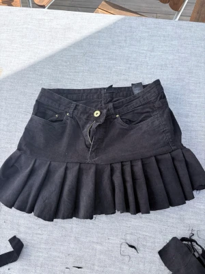 Svart plisserad minikjol från H&M - Svart kortkjol från H&M i manchestertyg med plisserad nederdel och klassiska jeansdetaljer som fickor och knapp. Ett par byxor innan som jag har sytt om till kjol