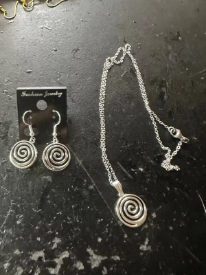 Silverset spiral örhängen & halsband - Snyggt set med örhängen och halsband i silverfärgad metall. Både örhängena och halsbandet har en spiralformad design som ger en cool och modern look. Perfekt för dig som gillar unika detaljer och vill sticka ut lite extra.