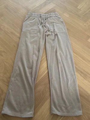 Beige mjukisbyxor från 157 - Säljer ett par beige mjukisbyxor från 157 i storlek XS. Byxorna har raka ben, resår i midjan med dragsko och två stora fickor framtill. Tillverkade i mjukt och skönt material som passar perfekt för chill dagar.