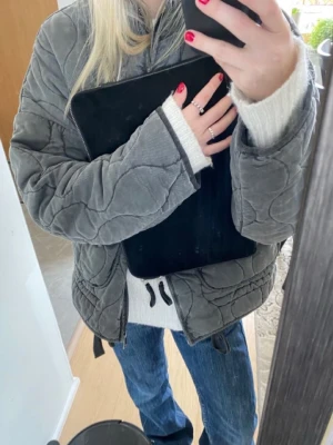 Grå quiltad pufferjacka - Säljer en grå populär quiltad pufferjacka med hög krage och dragkedja framtill. Den är från Zara och är helt slutsåld. Jackan har oversized passform, stora fickor och justerbar nederkant med snörning. Perfekt för kalla dagar och ger en cool, avslappnad look. Kan acceptera även prisförslag.