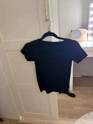 Svart ribbad topp med kort ärm - En svart ribbad topp med korta ärmar och fyrkantig ringning. Snygg och enkel modell som passar till mycket. Materialet är stretchigt och följsamt för en bekväm passform.
