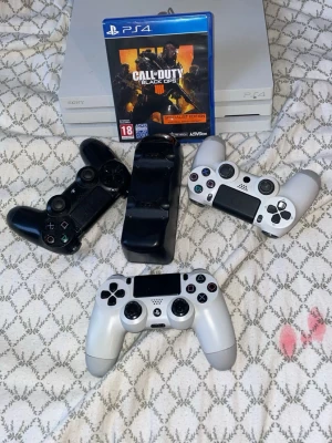 Vit PlayStation 4 Pro med 3 kontroller - Säljer en vit PlayStation 4 Pro med tre DualShock 4-kontroller (två vita, en svart), laddstation och spelet Call of Duty: Black Ops 4. Konsolen har en stilren design i plast och matchande kontroller. Perfekt för gamingkvällar med vänner!