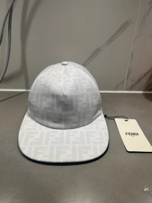 Vit keps från F - Snygg vit keps från F med det klassiska FF-monogrammet ton-i-ton över hela kepsen. Kepsen har böjd skärm och är tillverkad i ett slitstarkt tygmaterial. Perfekt accessoar för att lyfta din streetwear-look.