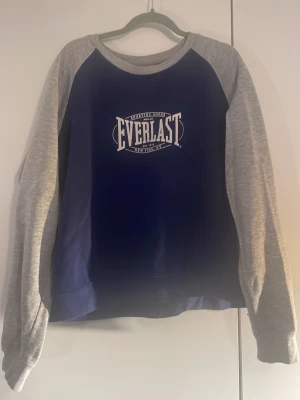 Everlast sweatshirt  - Mörkblå sweatshirt från Everlast med ljusgrå raglanärmar och vitt tryck på bröstet. Rund halsringning och avslappnad passform. Hör av er vid frågor 🫶 ps skulle säga att storleken är mer som s