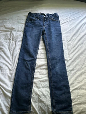 Blå skinny/slim fit jeans från Levi's - Säljer ett par klassiska blå jeans från Levi's med rak passform. Jeansen har normal midja, dragkedja och knapp framtill samt ikoniska bakfickor med Levi's-logga. Tillverkade i slitstark denim som passar till det mesta.