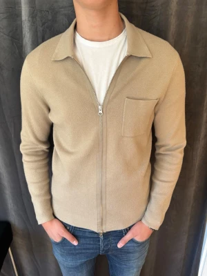 Beige ziptröja med krage - Snygg beige ziptröja med krage och bröstficka från Samsøe. Tröjan har lång ärm och är tillverkad i ett mjukt, stickat material som ger en clean och stilren look.