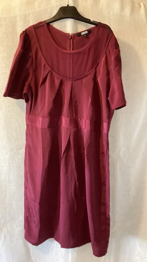 Vinröd kort klänning med kort ärm - Vinröd klänning i enkel och stilren design med korta ärmar och rund halsringning. Klänningen har en markerad midjesöm och är tillverkad i ett mjukt, lätt tyg som ger ett fint fall. Perfekt för dig som gillar minimalistisk stil.