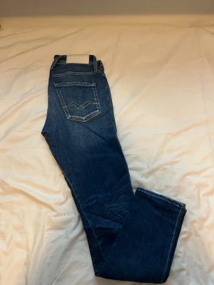 Mörkblå jeans från Replay - Säljer ett par mörkblå jeans från Replay med klassisk femficksdesign och raka ben. Jeansen har en snygg tvätt och detaljerade sömmar på bakfickorna. Tillverkade i slitstarkt denimtyg med en vit Replay-lapp bak i midjan.