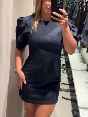 Mörkblå jeansklänning från Zara - Trendig mörkblå kort jeansklänning från Zara med puffärmar och figurnära passform. Klänningen har rund halsringning och är sydd i ett stretchigt jeanstyg som ger en snygg siluett. Perfekt för dig som vill ha en cool och modern look. Klänningen är oanvänd med prislapp. Säljs pga passar inte. 