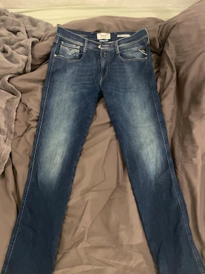 Mörkblå Replay jeans slim fit - Snygga mörkblå jeans från Replay med smal passform och klassiska fem fickor. Jeansen har slitningar och ljusare partier framtill. Tillverkade i denim med detaljerade sömmar och Replay-lapp bak i midjan. Finns inga defekter 