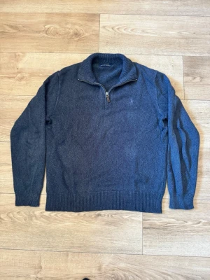 Blå stickad halvzip från Polo Ralph Lauren - Mörkblå stickad tröja från Polo Ralph Lauren med halvzip och diskret broderad logga på bröstet. Tröjan har ribbade muddar vid ärmslut och nederkant samt hög krage. Perfekt för lager på lager och en chill look. Tidigare ägaren har tagit bort tagsen därav priset 