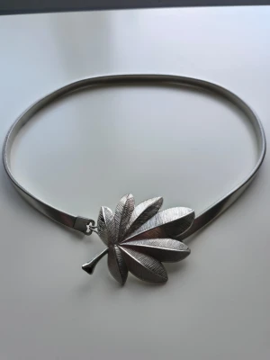 Silvrigt bälte med lövdetalj - Unikt bälte i silverfärgad metall med ett stort dekorativt löv som spänne. Bältet har en smal, stilren design. Lövet har fina detaljer som ger ett exklusivt intryck. 