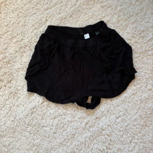 Svarta loose shorts med resårmidja - Svarta shorts med loose passform och bred resår i midjan. Lätta och luftiga, perfekta för varma dagar. Tillverkade i ett mjukt material som känns skönt mot huden. Enkla att matcha med olika toppar för en avslappnad stil.