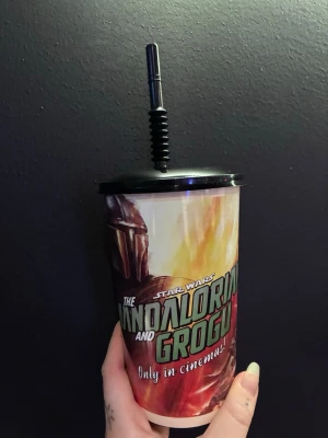 Star Wars Mandalorian plastmugg - ALDRIG ANVÄND Cool plastmugg med lock och sugrör från Star Wars: The Mandalorian and Grogu. Muggen har färgstarkt tryck med Mandalorian och actionmotiv, samt texten 'Only in cinemas!'. Perfekt för fans av serien och samlare. 