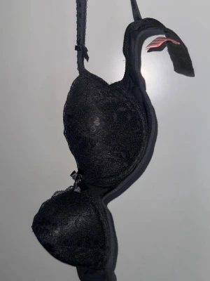 65C Svart spets-bh från Hunkemöller - Snygg svart bh från Hunkemöller med vadderade kupor och spetsdetaljer. Axelbanden är justerbara och det finns små rosetter framtill. Perfekt för dig som gillar en klassisk och elegant look.