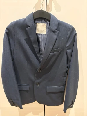 Marinblå Kavaj  - Säljer en Zara boys, marinblå kavaj med fina ärm knappar och en fin krage, värmer bra och har en bröstfick du kan välja med att ha något i eller inte. Mer information är bara att säga till om.