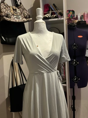 Mintgrön omlottklänning – H&M – strl XS - Stilren och feminin ljusgrön omlottklänning från H&M. Klänningen har en smickrande V-ringning och knytning i midjan som skapar en fin siluett. Det mjuka och följsamma tyget gör klänningen bekväm att bära och perfekt för både vardag, sommar och mer uppklädda tillfällen