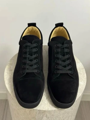 Svarta Louboutin i mocka - Dessa Louboutin-skor utstrålar tidlös elegans i sin enkelhet. Den djupa, svarta mockan omsluter foten med en mjuk och lyxig känsla, medan den ikoniska röda sulan diskret skvallrar om skons exklusiva ursprung. En sofistikerad siluett utan onödiga detaljer gör dessa skor till en mångsidig följeslagare, lika passande för en elegant kväll som till en sofistikerad vardagslook."