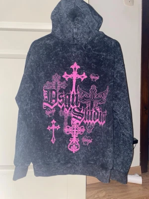 Hoodie med tryck från Boohoo - Cool svart hoodie från Boohoo med acid wash-effekt och stora rosa kors och logotyp på ryggen. Hoodien har en rymlig huva och ribbade muddar. Perfekt för dig som gillar streetwear och grafiska prints. Storlek S