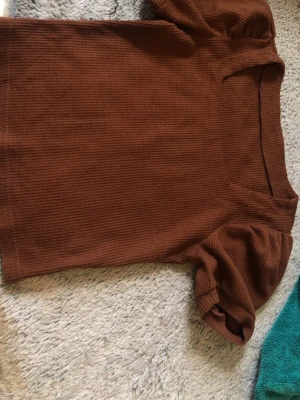 Brun ribbad topp med puffärm - Snygg brun ribbad topp med korta puffärmar och v-ringning. Toppen har en figurnära passform och är tillverkad i ett mjukt, stretchigt material som känns bra. Skriv privat om ni vill se den på, pris kan diskuteras ❤️