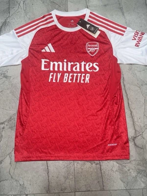 Arsenal matchtröja Saka 7 Adidas röd/vit - Arsenal hemmatröja från Adidas med Saka 7 på ryggen. Tröjan är röd med vita ärmar, har klubbmärke och sponsortryck framtill samt Premier League-logga. Tillverkad i lätt och ventilerande Aeroready-material, perfekt för fotbollsträning eller match.