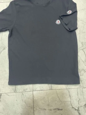 Svart Moncler t-shirt med logga - Snygg svart t-shirt från Moncler med klassisk rund hals och två broderade Moncler-loggor på bröstet och ärmen. Tillverkad i mjuk bomull och har en clean, stilren look som passar perfekt till jeans eller shorts.