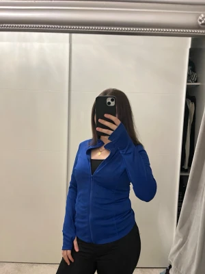 Blå gymkofta från Shein  - Snygg kornblå ziptröja med hög krage och långa ärmar. Tröjan har en hel dragkedja framtill och är tillverkad i ett mjukt, stretchigt material som passar perfekt till en sportig eller avslappnad stil.