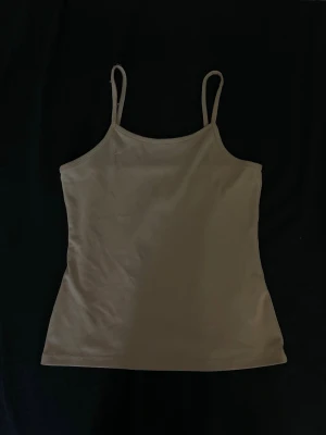 Beige linnetopp med smala axelband - Säljer en enkel och stilren beige linnetopp med smala axelband. Toppen har en rak passform och ärmlös design, perfekt att matcha med jeans eller kjol. Materialet känns mjukt och lätt, vilket gör den bekväm att bära under varma dagar.