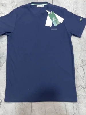 Mörkblå t-shirt från Lacoste - Snygg mörkblå t-shirt från Lacoste i ekologisk bomull. Klassisk rund halsringning och diskret Lacoste-logga på bröstet. Perfekt basic-plagg med stilren design och korta ärmar. Passar till allt och har en clean look.