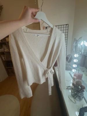 Vit omlottkofta med knytband - Mysig vit kofta med knytband i midjan och långa ärmar från Gina.