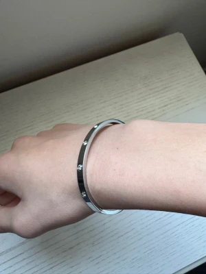Silverfärgat armband med stenar - Snyggt och stilrent armband i silverfärgad metall med infattade klara stenar runt om. Armbandet har en slät, rundad form och ger en modern och elegant känsla. Perfekt för dig som gillar minimalistiska accessoarer med lite extra bling.