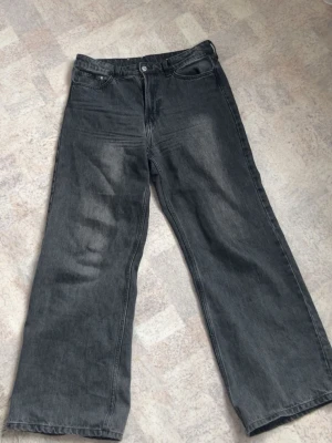 Gråa wide leg jeans - Säljer ett par gråa wide leg jeans med hög midja. Jeansen har en avslappnad passform och är tillverkade i denim med lätt tvättad look. Perfekta för en trendig och bekväm stil. Storlek 40-42