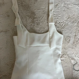 Vit topp med knyt från Zara - Supersnygg vit topp från Zara med breda axelband som knyts upptill. Stilren design med fyrkantig urringning och figurnära passform. Materialet är slätt och känns lyxigt mot huden, perfekt för dig som gillar minimalistisk stil. Storlek S, använd endast en gång så i super bra skick!