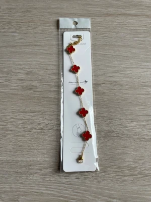 Armband - Snyggt armband i guldfärg med fem röda fyrklöverformade hängen. 