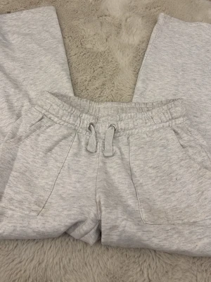 Ljusgrå mjukisbyxor från 157 - Ljusgrå mjukisbyxor från 157 med resår och dragsko i midjan. Byxorna har två sidofickor och är tillverkade i mjukt, fleeceliknande material. Perfekta för en chill och avslappnad stil.