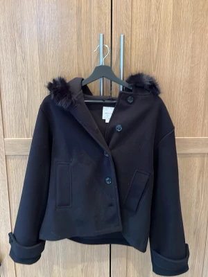 Svart kappa med fuskpäls från Gina Tricot - Stilren svart kappa från Gina Tricot med fuskpälsdetaljer på huvan. Pälsen går att ta av och på. Passar perfekt nu till våren och sommaren då den inte är så tjock💞Säljer då den inte kommer till användning, använd ett fåtal gånger🥰Passar som S!! Buda gärna!!