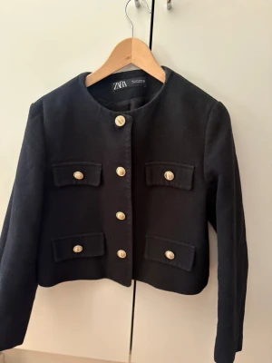 Svart kavaj med guldknappar från Zara - Stilren svart kavaj från Zara med rund halsringning och dekorativa guldknappar framtill.  Nypris: 400kr